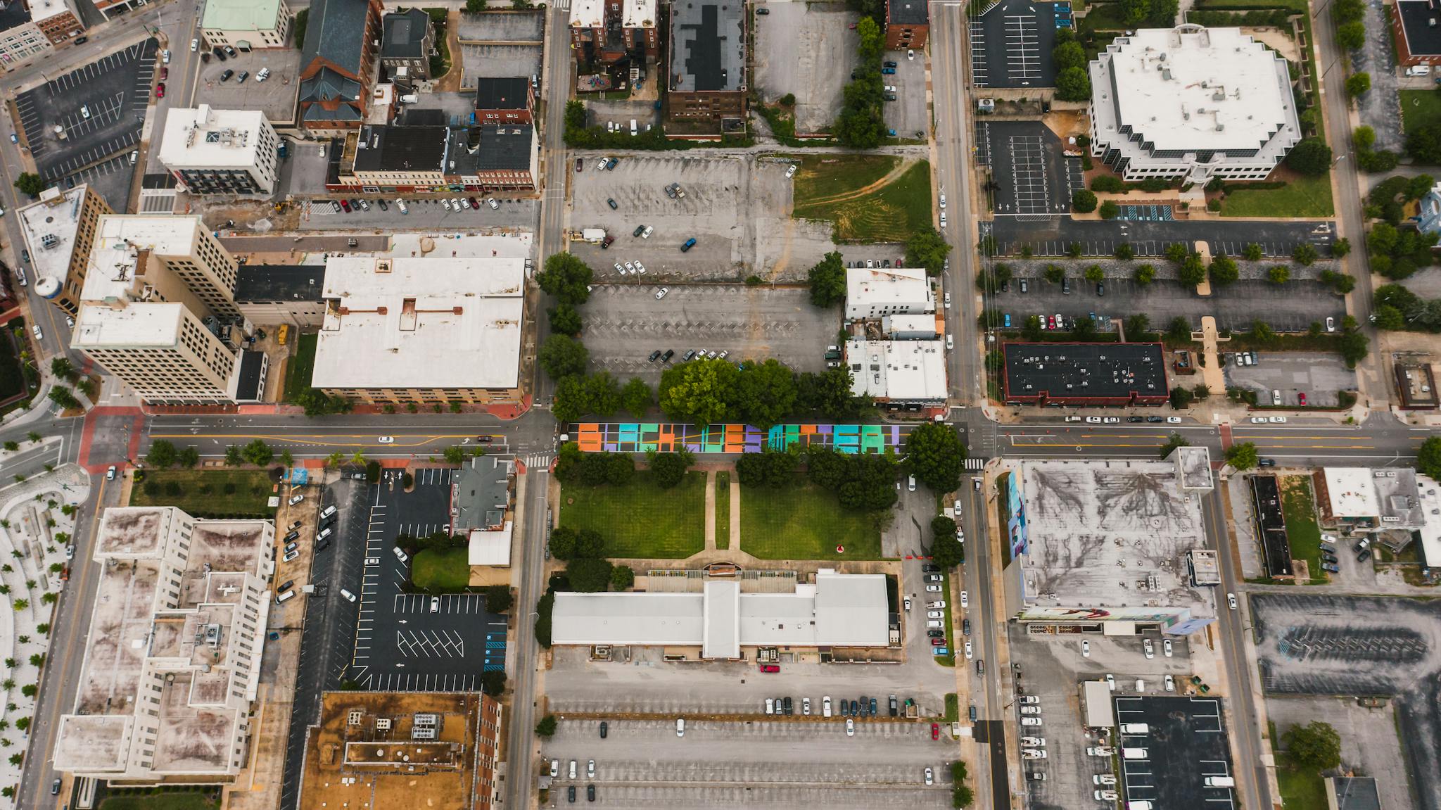 Drone view of building roofs near roadway with bright Black Lives Matter inscription near city parking with vehicles in daylight
