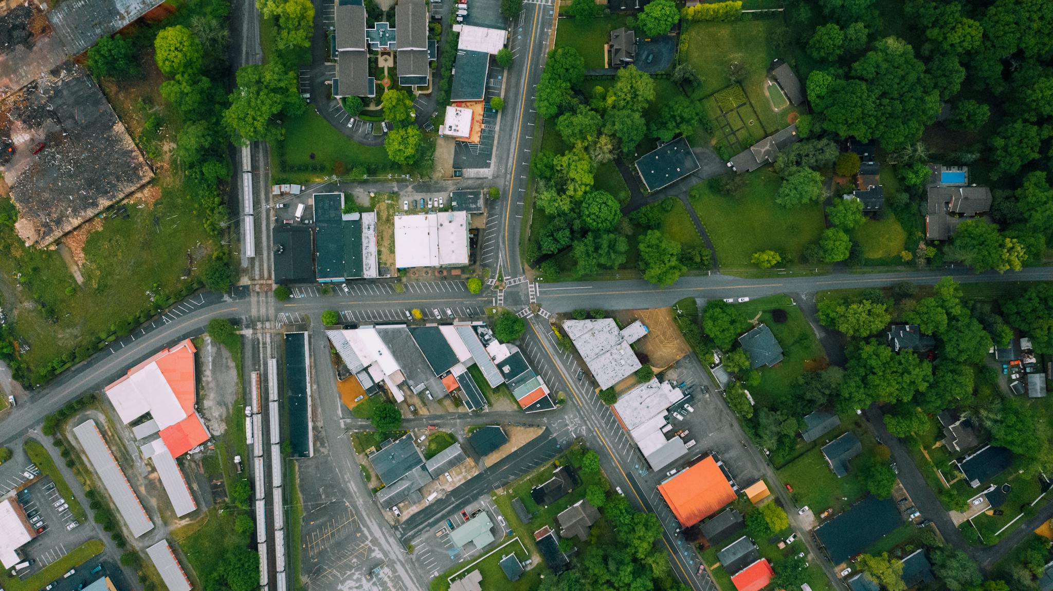 Drone view outpost town district with contemporary cottages and large industrial buildings surrounded with lush tree on summer day